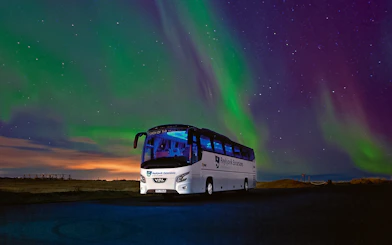 Tour bus under Northern Lights in Iceland's night sky.