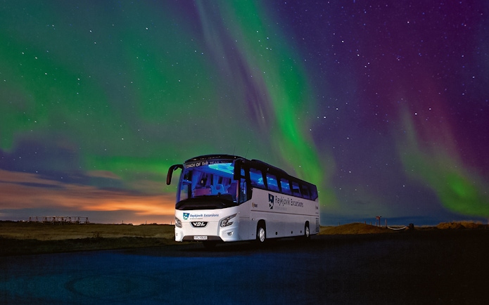 Tour bus under Northern Lights in Iceland's night sky.