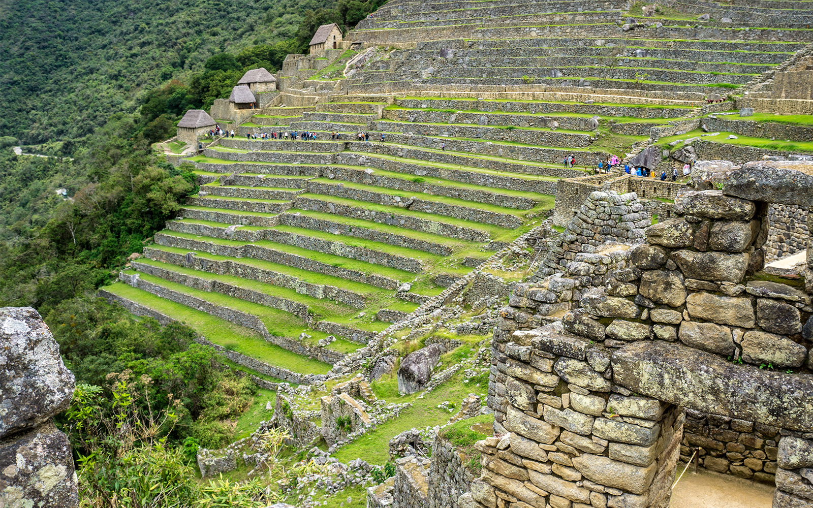 Terraced stone structures at Machu Picchu, Peru, with tourists exploring the ancient site.