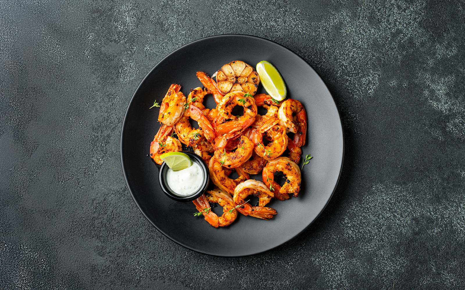 Grilled shrimp with lime and sauce on a black plate, Jimbaran Bali seafood dinner.