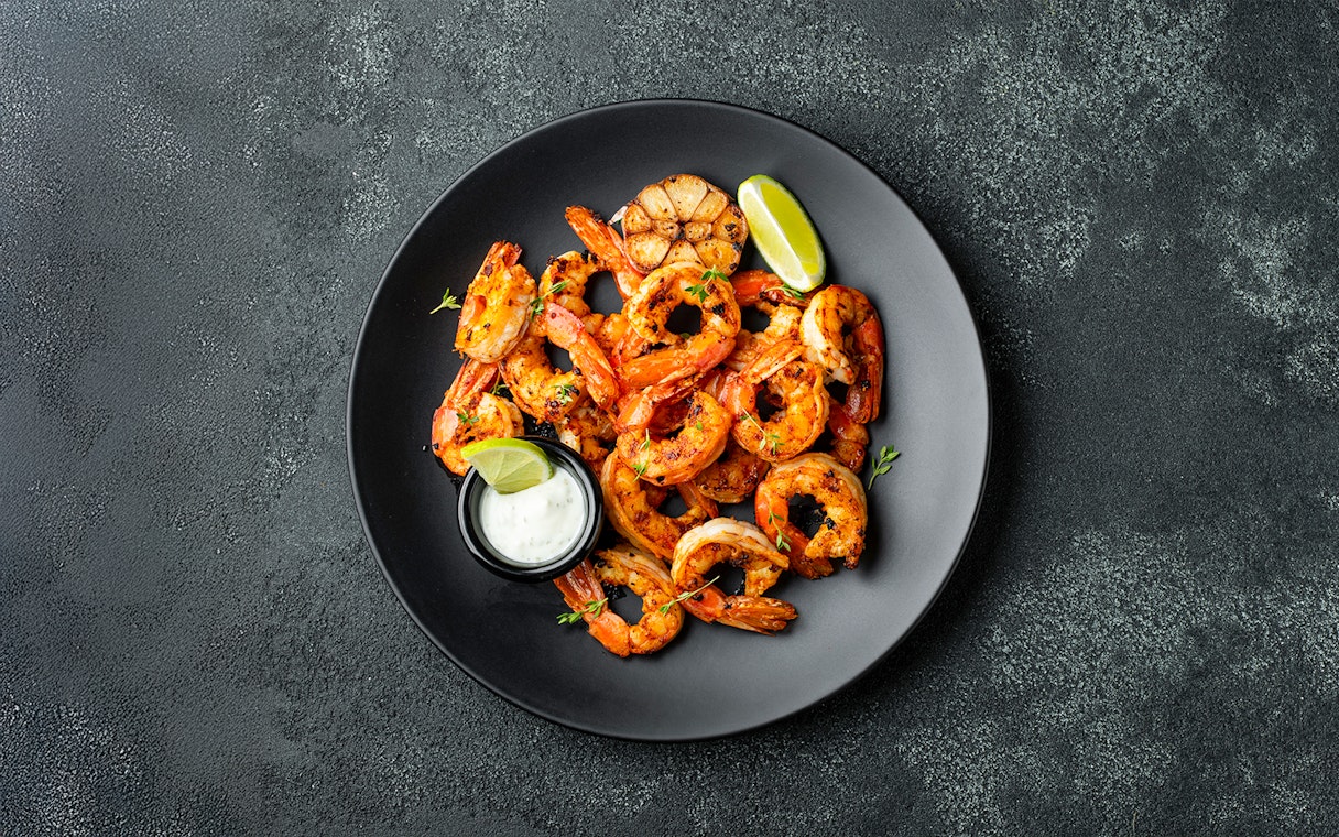 Grilled shrimp with lime and sauce on a black plate, Jimbaran Bali seafood dinner.