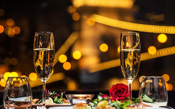 Champagne glasses and dinner setting on Budapest dinner cruise with city lights.