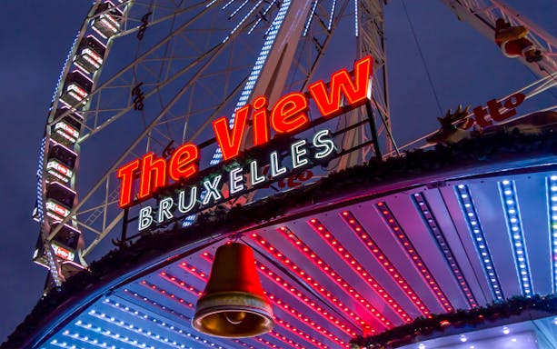 Ferris wheel with "The View Bruxelles" sign illuminated at dusk in Brussels.