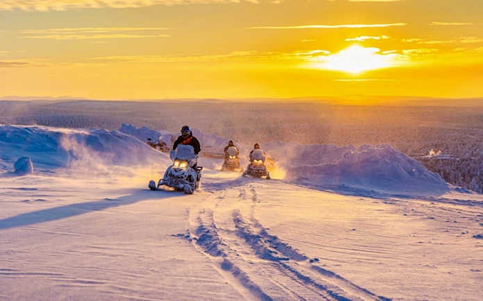 Snowmobilers riding through snowy landscape at sunset during Rovaniemi safari adventure.