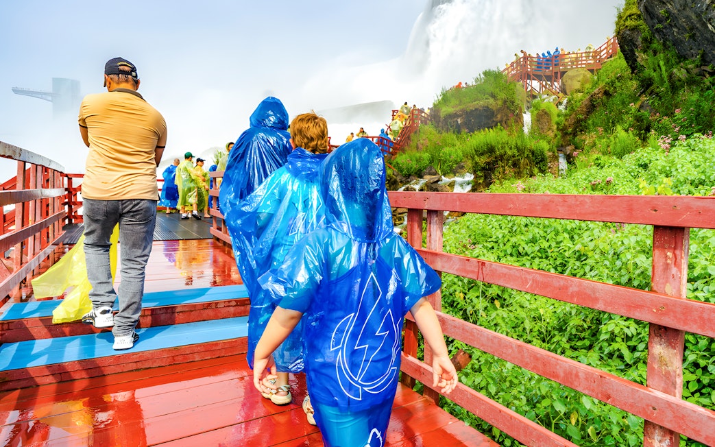 Visitors in blue ponchos walking on a wooden walkway near Niagara Falls.
