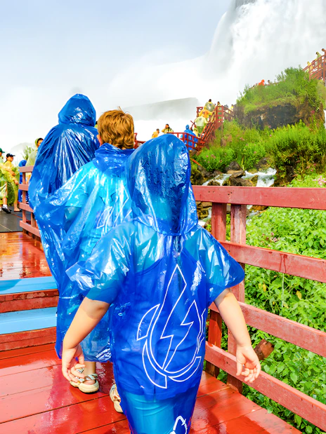 Visitors in blue ponchos walking on a wooden walkway near Niagara Falls.