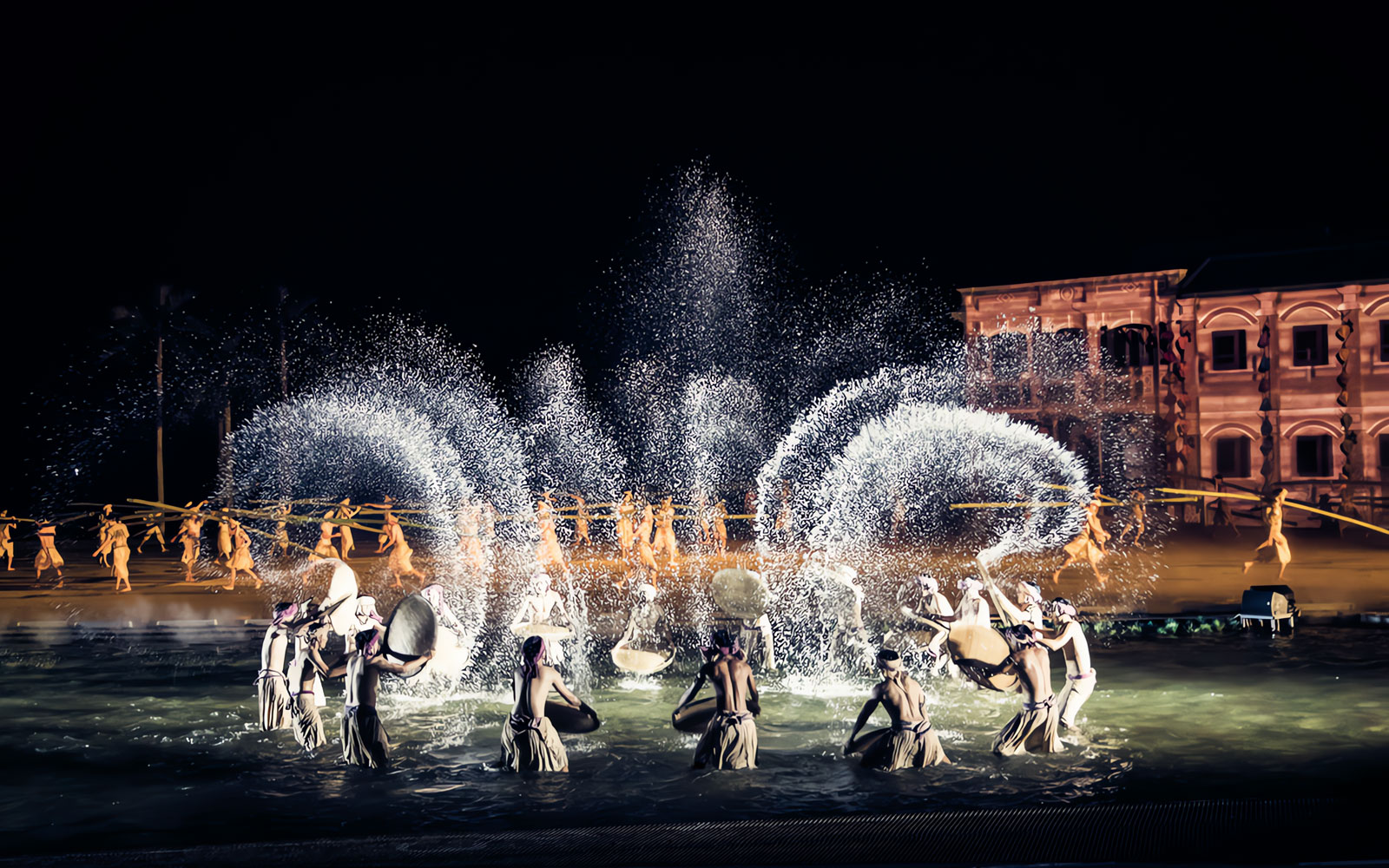 Performers in traditional attire during Hoi An Memories Show, Vietnam, with water effects and historical backdrop.