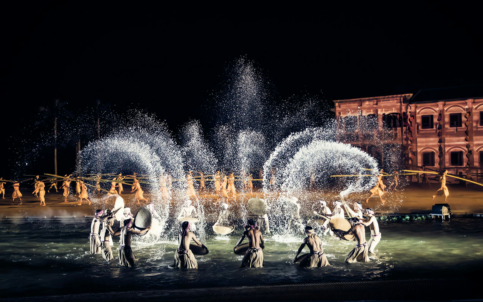 Performers in traditional attire during Hoi An Memories Show, Vietnam, with water effects and historical backdrop.