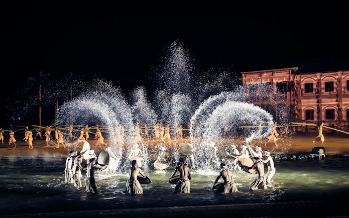 Performers in traditional attire during Hoi An Memories Show, Vietnam, with water effects and historical backdrop.