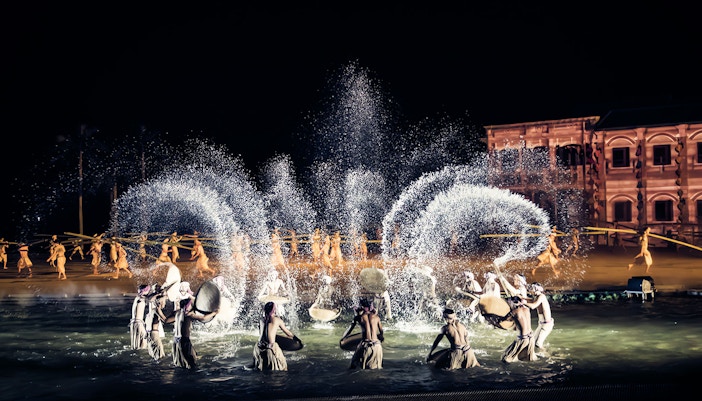 Performers in traditional attire during Hoi An Memories Show, Vietnam, with water effects and historical backdrop.