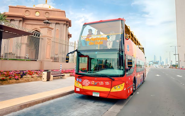 City Sightseeing hop-on hop-off bus in Abu Dhabi near a historic building.