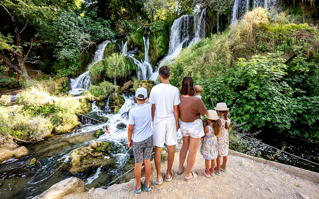 Family observing Kravica Waterfalls surrounded by lush greenery.