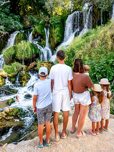 Family observing Kravica Waterfalls surrounded by lush greenery.