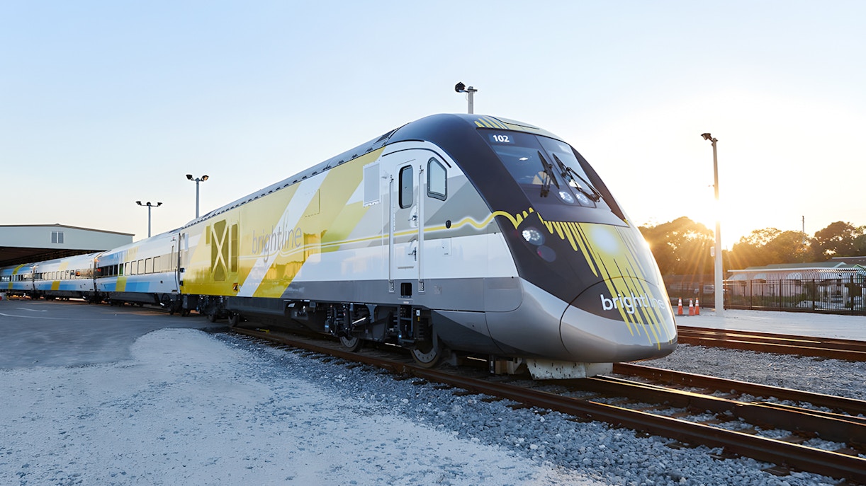 Brightline train exterior on tracks at sunset.
