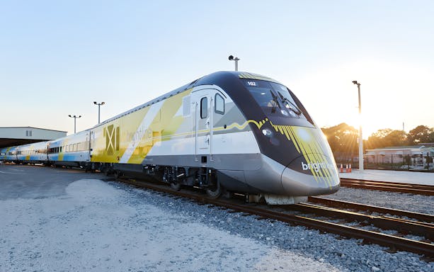 Brightline train exterior on tracks at sunset.