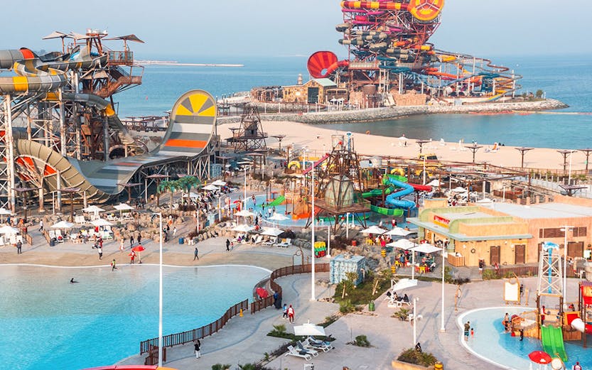 Aerial view of colorful water slides and pools at Meryal Waterpark by the sea.