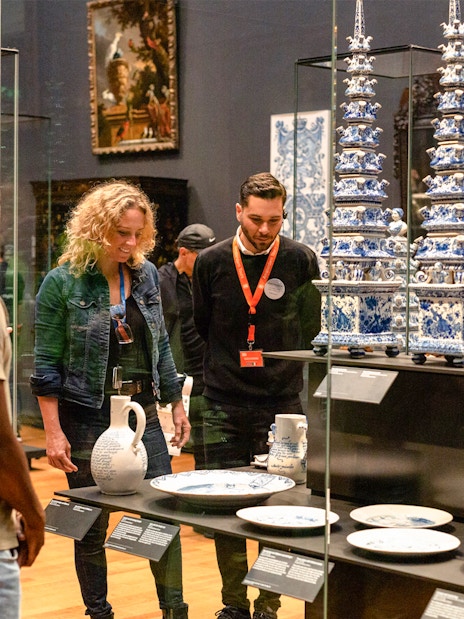 Visitors observing Delftware pottery on a guided tour at the Rijksmuseum, Amsterdam.