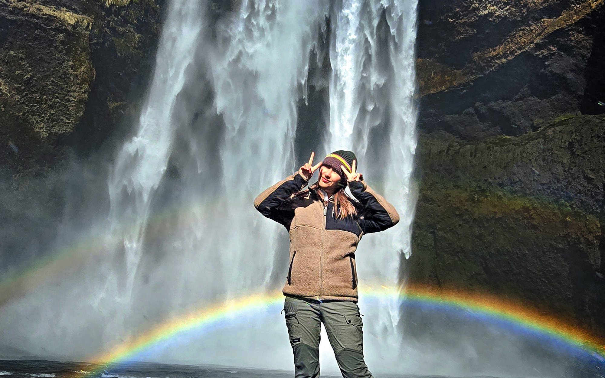 Tourist posing with rainbow at Skógafoss waterfall, Reykjavik.