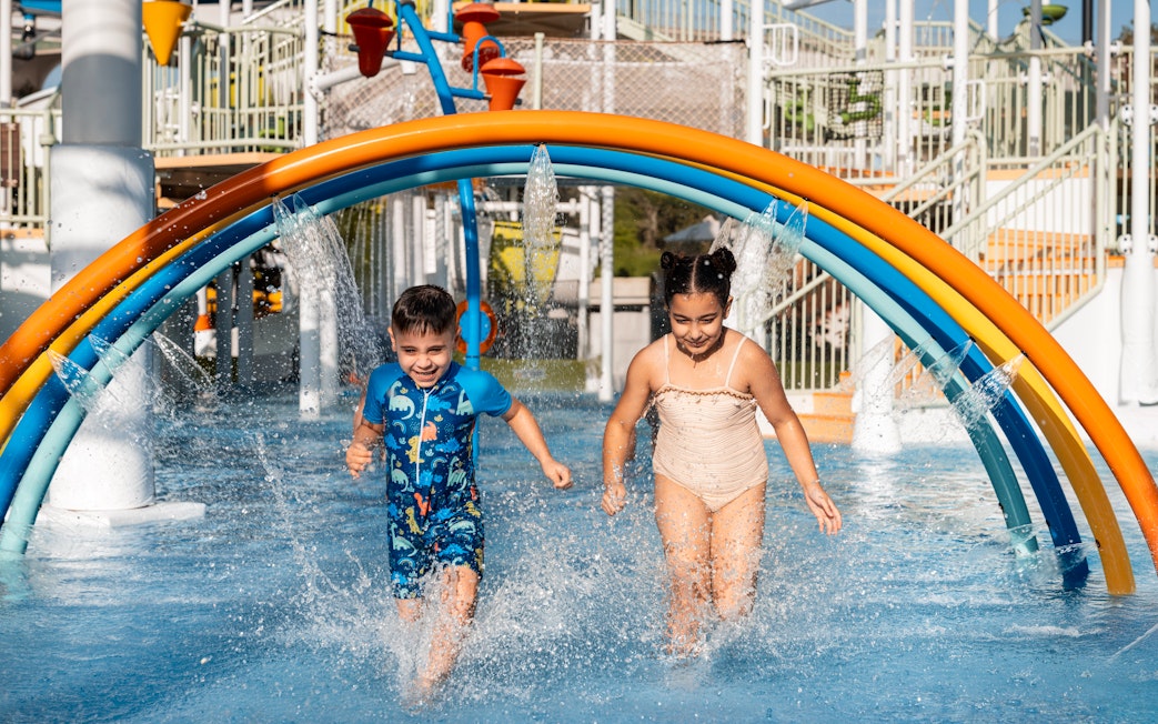 Children enjoying rainbow water arches at Grand Hyatt waterpark, Dubai.