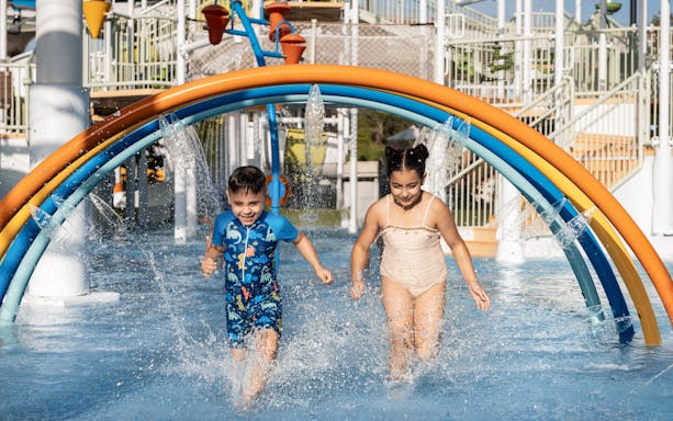Children enjoying rainbow water arches at Grand Hyatt waterpark, Dubai.