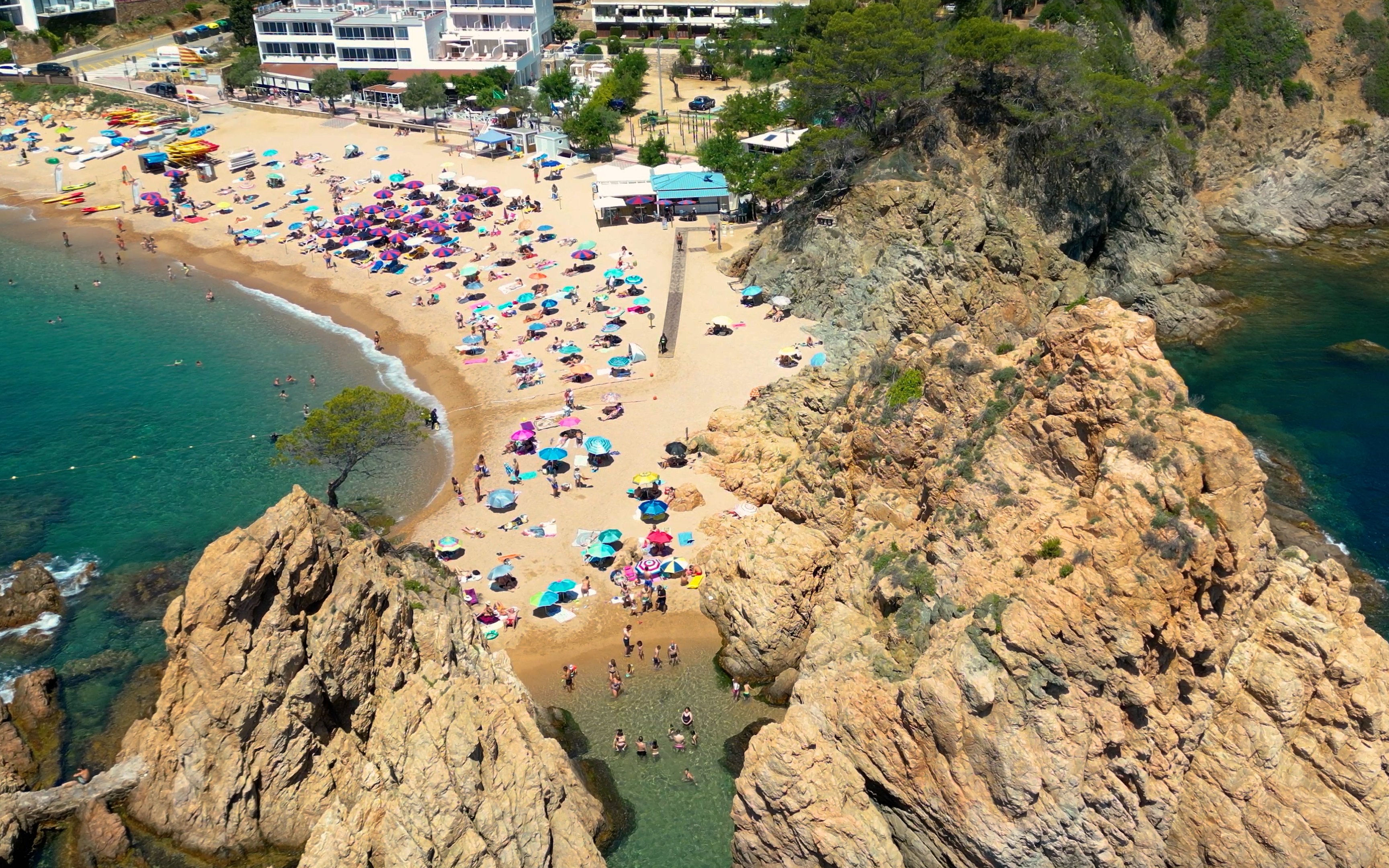 Tossa de Mar Beach with colorful umbrellas and rocky cliffs.