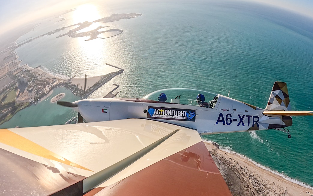 Aerobatic plane flying over coastal landscape during GFORCE Aerobatic Passenger Experience.