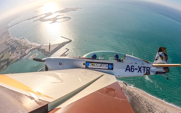 Aerobatic plane flying over coastal landscape during GFORCE Aerobatic Passenger Experience.