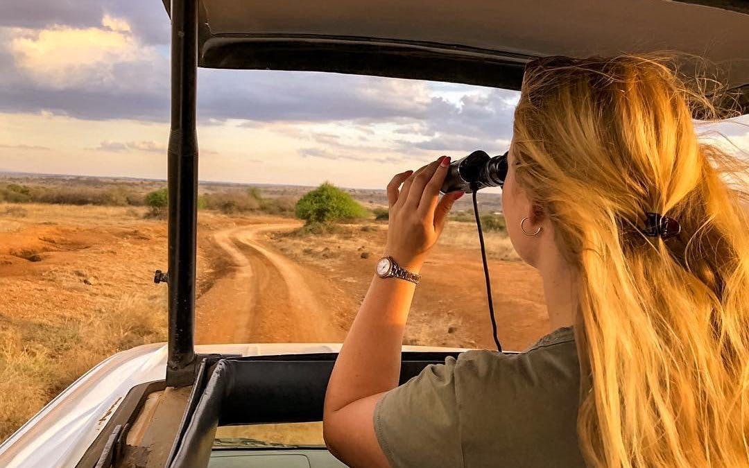 Safari vehicle on dirt road in Nairobi National Park, person using binoculars to view wildlife.