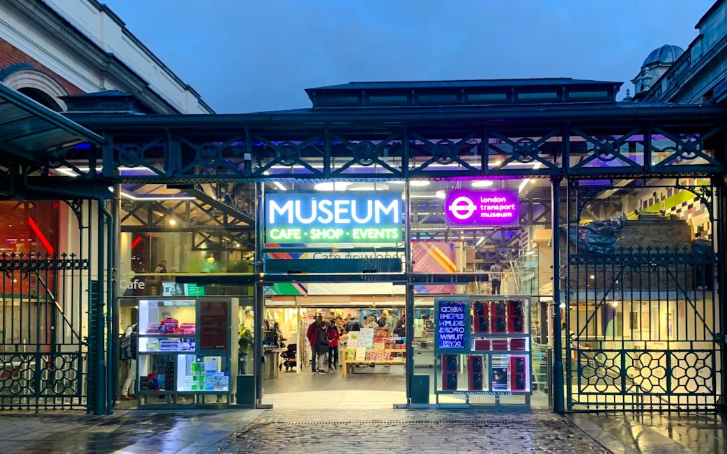 Entrance of the London Transport Museum with neon signs and visitors inside.