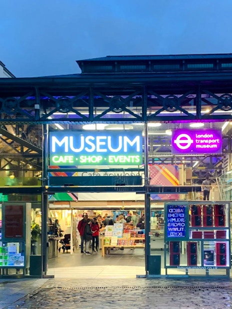 Entrance of the London Transport Museum with neon signs and visitors inside.