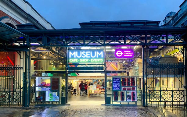 Entrance of the London Transport Museum with neon signs and visitors inside.