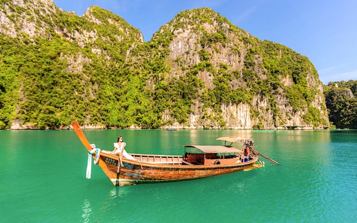 Longtail boat with woman enjoying view of Phi Phi Island cliffs and turquoise water.