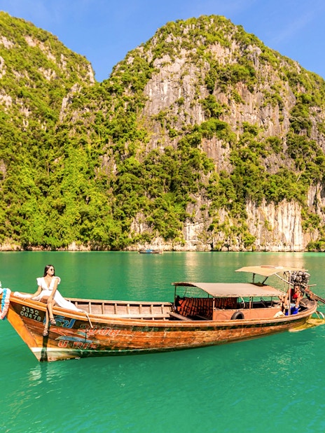 Longtail boat with woman enjoying view of Phi Phi Island cliffs and turquoise water.