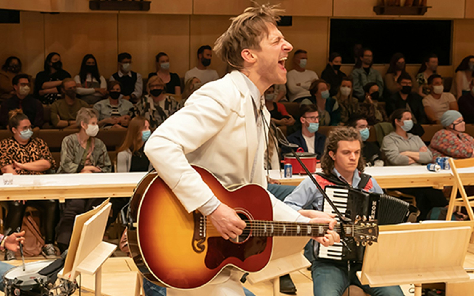 Performer playing guitar during Oklahoma! musical with audience in background.
