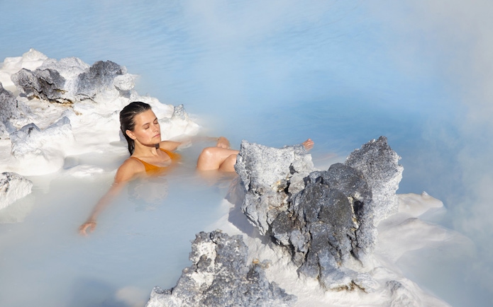 Tourist relaxing in Blue Lagoon, Iceland, surrounded by geothermal rocks.