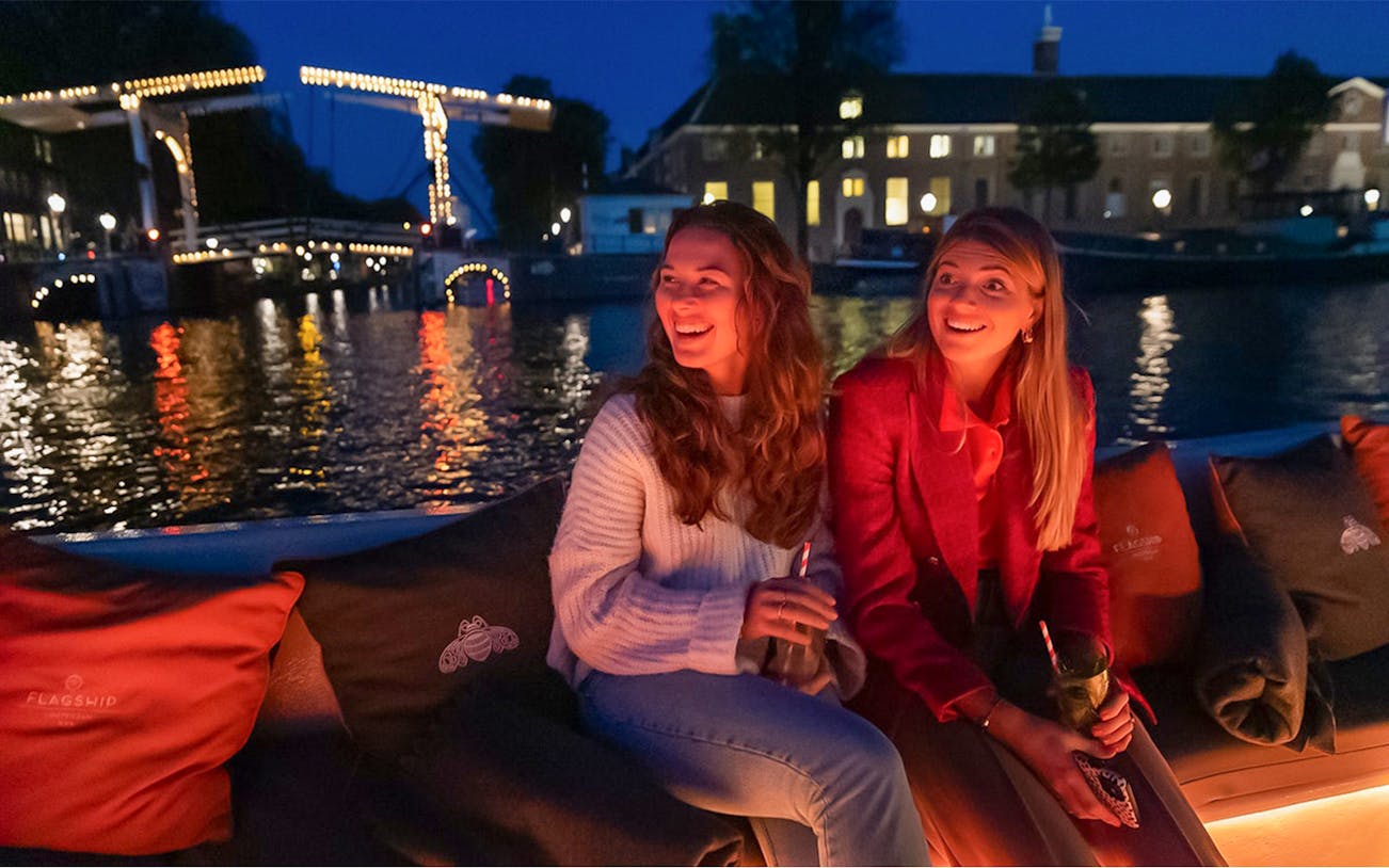 Evening canal cruise in Amsterdam's Red-Light District with illuminated bridge and open bar.