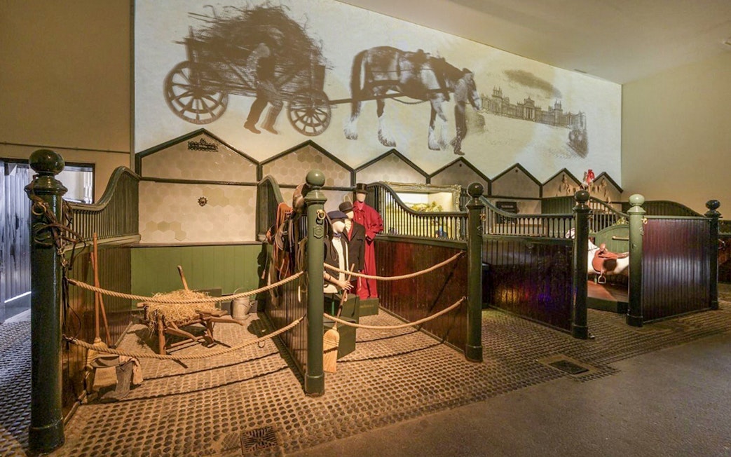 Blenheim Palace State Rooms exhibit with horse stables and historical carriage projection.