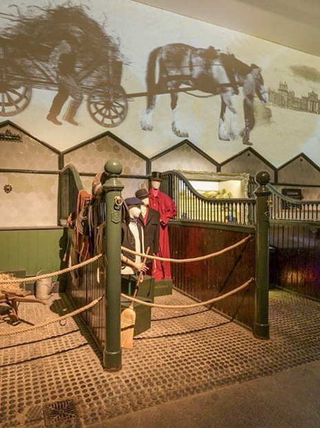 Blenheim Palace State Rooms exhibit with horse stables and historical carriage projection.