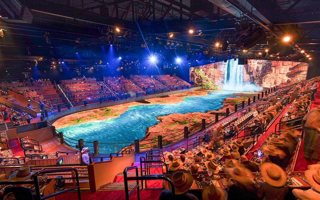 Audience watching Australian Outback Spectacular Heartland Dinner & Show with waterfall backdrop.