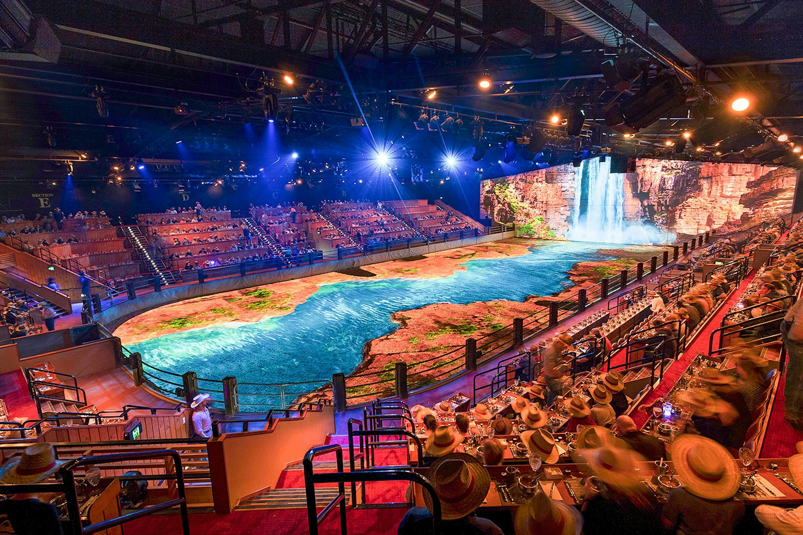 Audience watching Australian Outback Spectacular Heartland Dinner & Show with waterfall backdrop.
