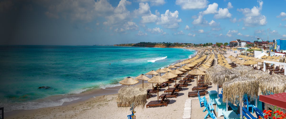 Sandy beach with straw umbrellas and sun loungers along the Black Sea coast in Constanta, Romania.