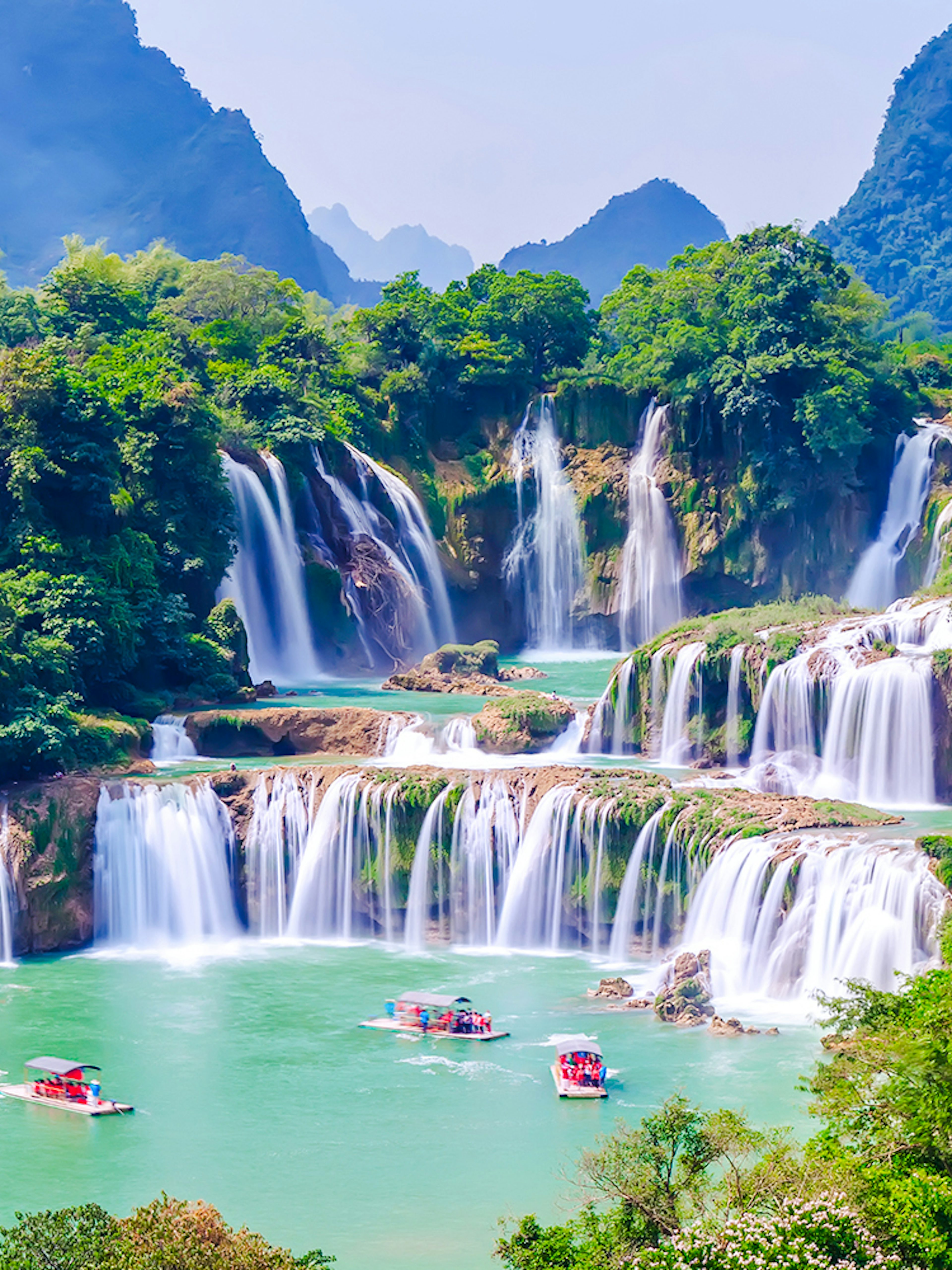 Boats on emerald waters near cascading waterfalls at Plitvice Lakes National Park.