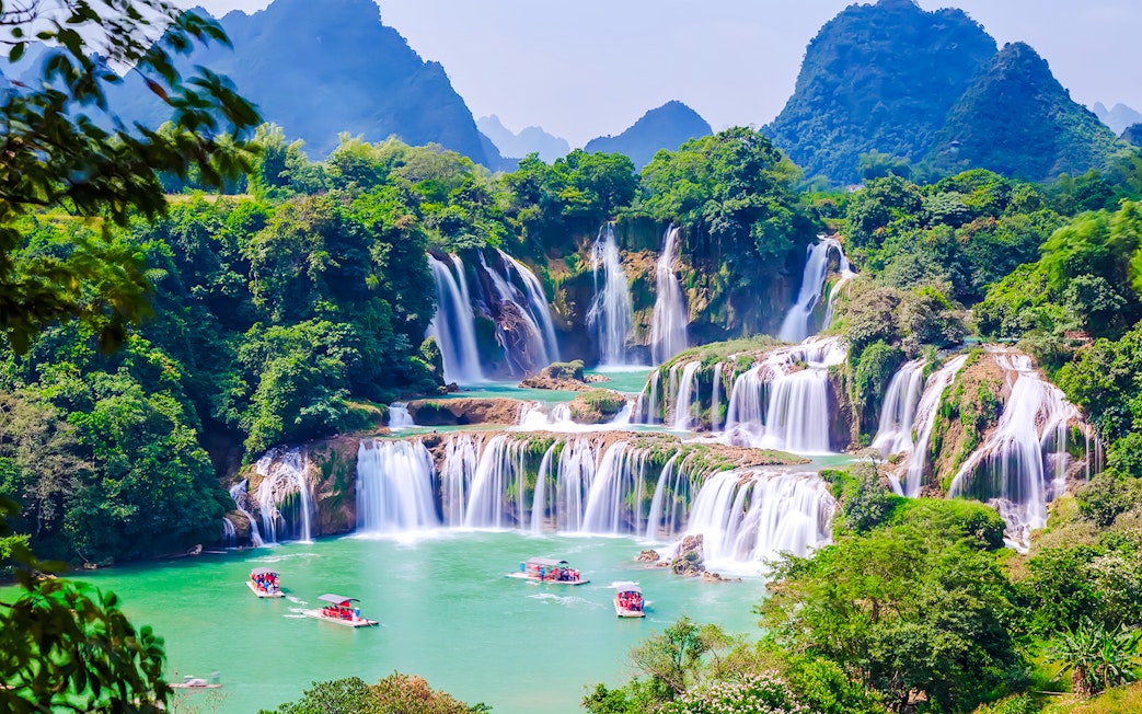 Boats on emerald waters near cascading waterfalls at Plitvice Lakes National Park.