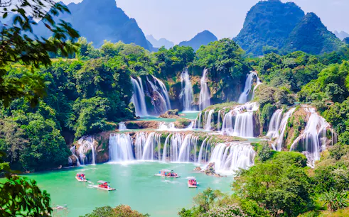 Boats on emerald waters near cascading waterfalls at Plitvice Lakes National Park.
