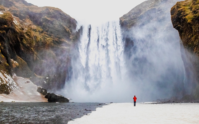 Person standing near Skogafoss waterfall in Iceland.