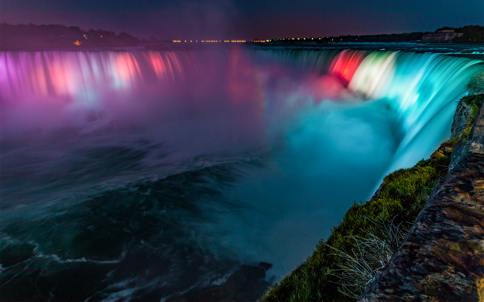 Niagara Falls illuminated by colorful lights during night show.
