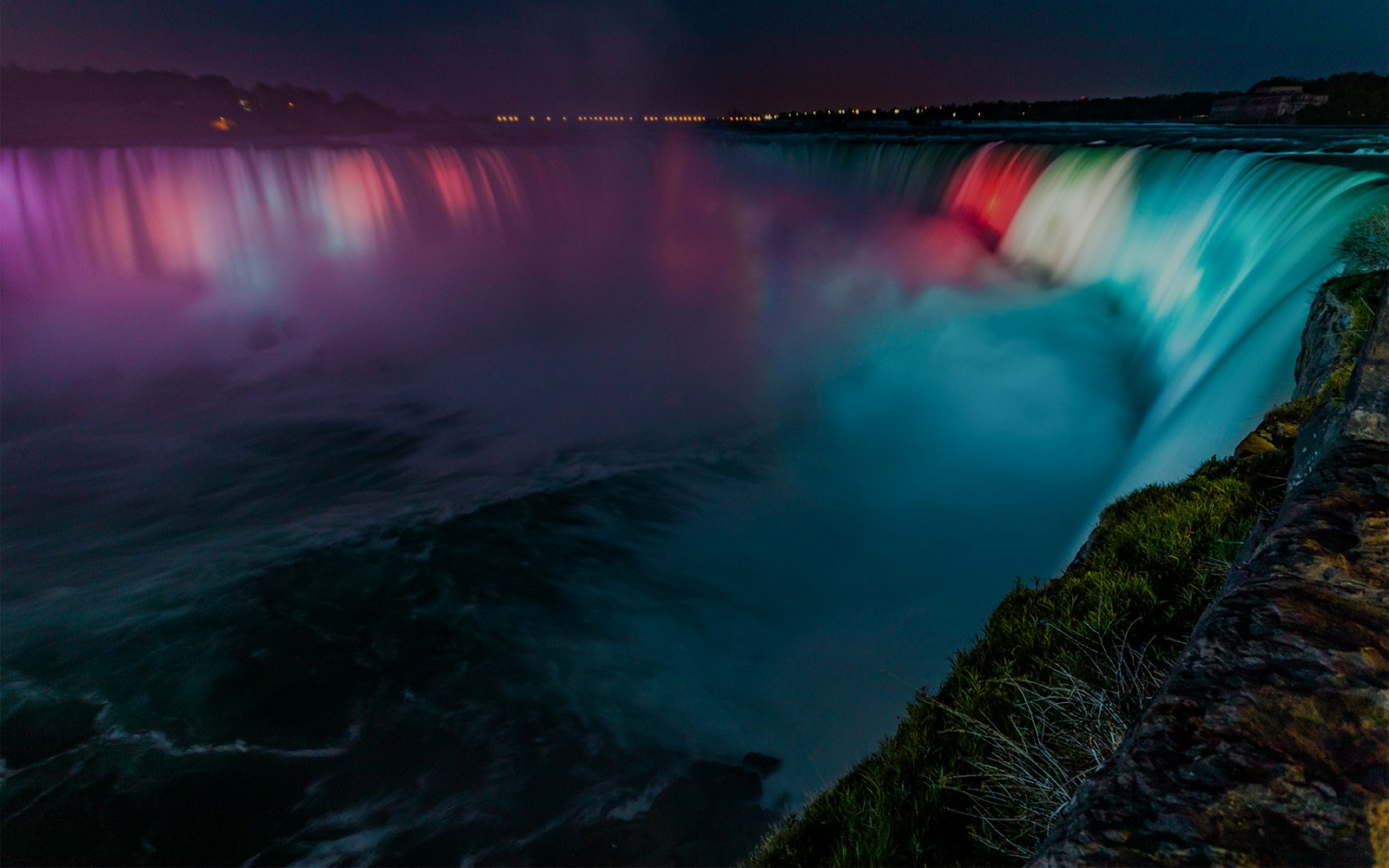 Niagara Falls illuminated by colorful lights during night show.
