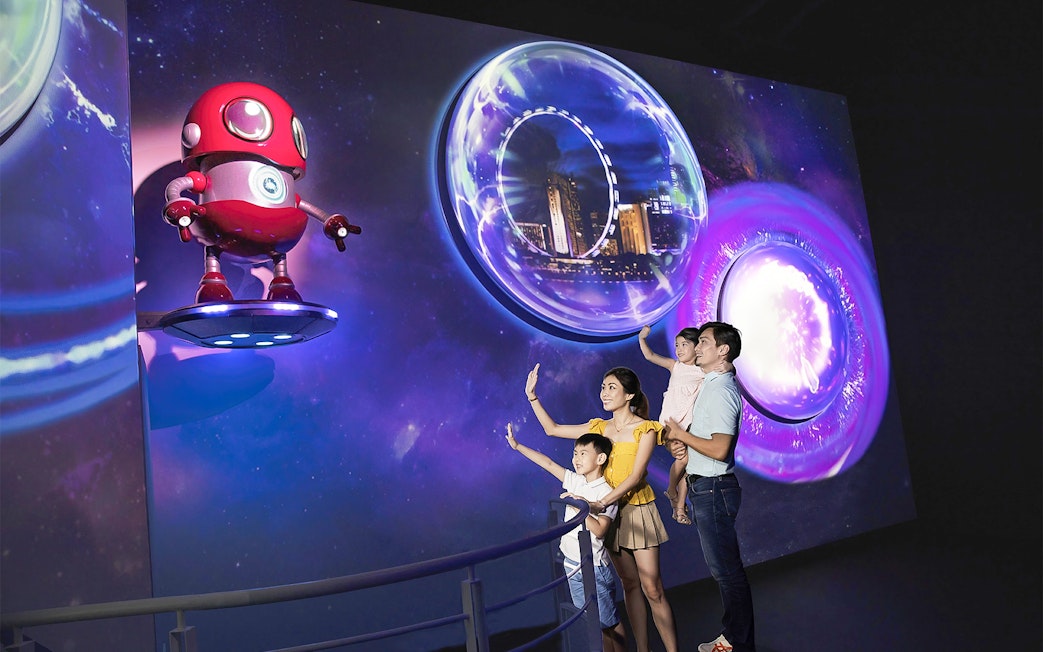 Family exploring Time Capsule exhibit at Singapore Flyer with futuristic visuals.