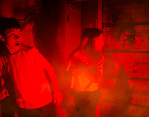 Friends exploring a dimly lit haunted house with eerie red lighting.