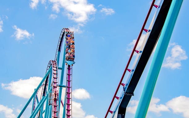 Riders on the Mako roller coaster at SeaWorld Orlando against a blue sky.